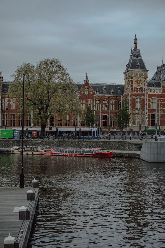 Scenic view of Amsterdam Central Station with canal boat and historic architecture.